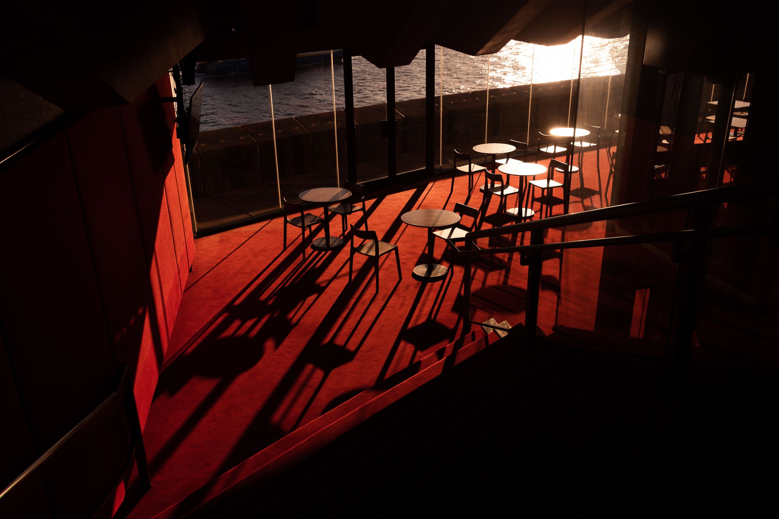 Image of a dining area, with sun setting through window in the background. Long shadows are cast across the red carpet.