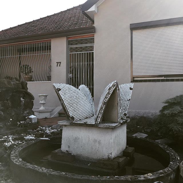 A strange statue resembling the Opera House sails sits in a garden out the front of a house